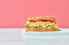 a sandwich with lettuce, tomato and chicken on a white plate against a pink background