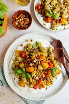 two white plates topped with different types of food next to bowls of nuts and vegetables