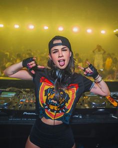 a woman with headphones on standing in front of a dj's equipment at a concert