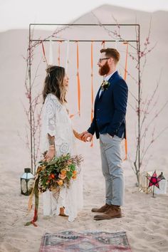 a man and woman standing in the sand holding hands