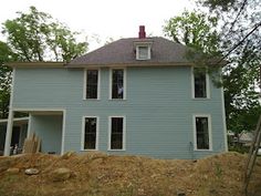 a large blue house sitting on top of a pile of dirt next to a forest