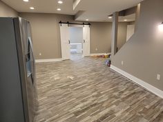 an empty kitchen and living room with wood flooring in the foreground, open door leading to another room