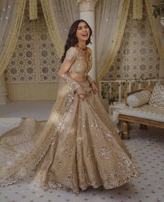 a woman in a gold and white bridal gown standing next to a bed with drapes on it