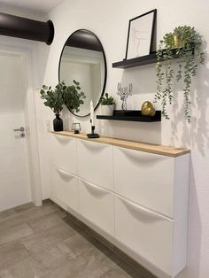 there is a mirror and some plants on the counter in this room with white walls