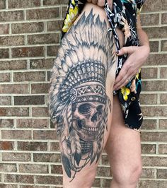 a man with a tattoo on his leg and headdress is standing in front of a brick wall