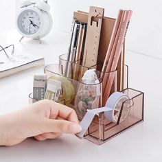 a person is holding a pen and paper in a holder on a desk next to an alarm clock