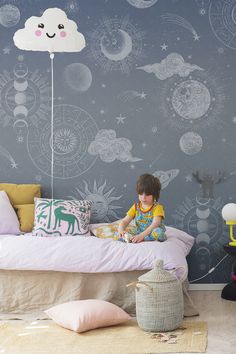 a child sitting on a bed in front of a wall with clouds and planets painted on it