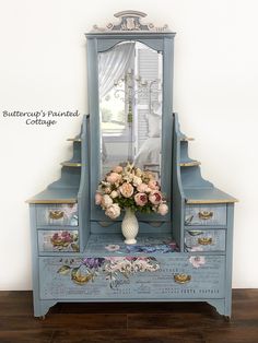 a blue dresser with flowers on it and a mirror