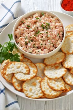 a white plate topped with crackers next to a bowl of dip and some parsley