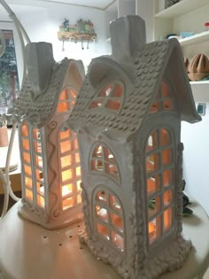 two white ceramic houses sitting on top of a table with candles in front of them