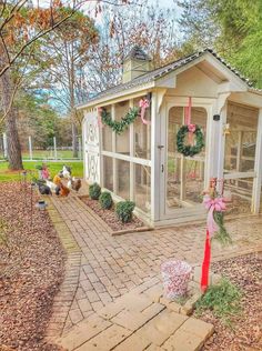 a small white chicken coop with wreaths on the door and windows in front of it