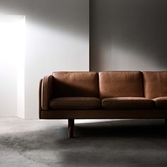 a brown leather couch sitting on top of a cement floor next to a white wall