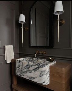 a marble sink in a bathroom with two lamps on the wall and a mirror above it