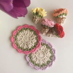 three crocheted coasters with flowers in them sitting on a table next to a purple flower