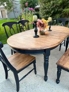 a wooden table with four black chairs and a vase filled with flowers on top of it