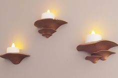 three candles are lit on the wall next to two scallop shaped candle holders