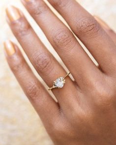 a woman's hand wearing a gold ring with an oval shaped diamond on it