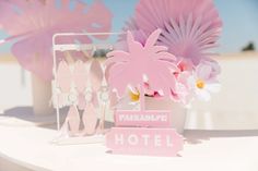 a pink hotel sign sitting on top of a white table next to flowers and fan