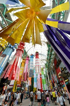 many people are walking through an indoor area with colorful ribbons hanging from the ceiling and glass windows