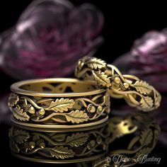 two gold wedding rings sitting next to each other on top of a black surface with pink flowers in the background