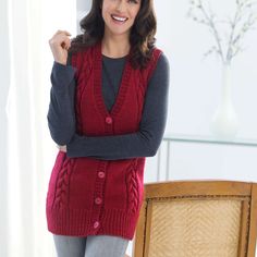 a woman standing in front of a chair wearing a red sweater and grey pants with her arms crossed