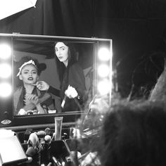 a black and white photo of two women in front of a mirror with lights on