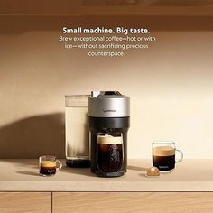 a coffee maker sitting on top of a wooden counter next to two cups of coffee