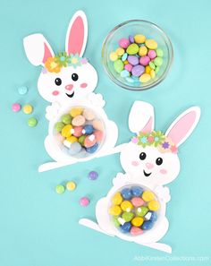 two bunny shaped candy bowls with candies in them on a blue surface next to a bowl of jelly beans