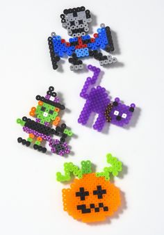 four perler bead halloween brooches on a white surface, one with an orange pumpkin and the other with a black cat