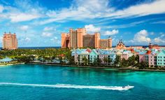 a boat traveling through the water near some buildings and palm trees in front of a body of water