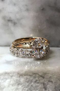 two wedding rings with diamonds on them sitting on a marble countertop in front of a marble background