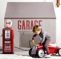 a little boy is playing with a toy car in front of an old gas station