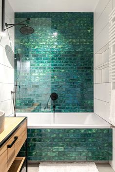 a bathroom with green tiles on the wall and bathtub next to it, along with a rug