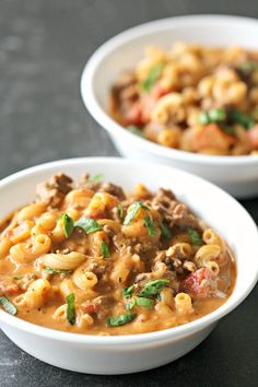 two white bowls filled with pasta and meat soup on top of a black countertop