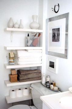 a white toilet sitting next to a bathroom sink under a mirror and shelves filled with towels