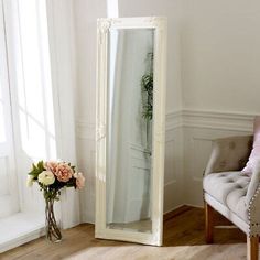 a large white mirror sitting in the corner of a room next to a chair and flower vase