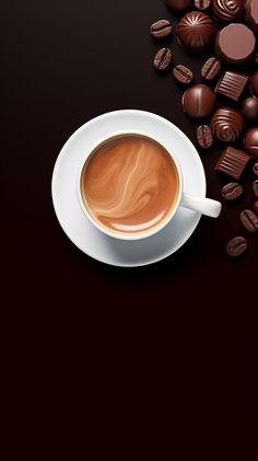 a cup of coffee and some chocolates on a black table with a dark background