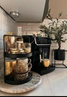 there is a coffee maker on the counter next to some cups and saucers in front of a potted plant