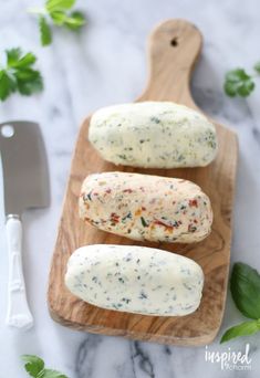 three hot dogs on a cutting board with cheese and herbs