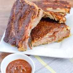 two pieces of meat sitting on top of a white plate next to a bowl of sauce