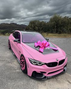 a pink car with a big bow on it's hood parked in a parking lot