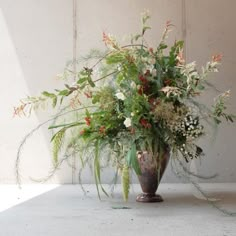 a vase filled with lots of flowers on top of a white floor next to a wall