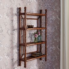 a wooden shelf with vases and books on it in front of floral wallpaper