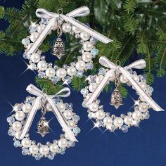 two christmas wreaths with bells and bows are hanging from a fir tree, decorated with crystal beads