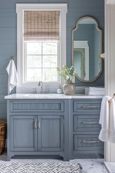 a bathroom with blue walls and white counter tops, an oval mirror above the double sink