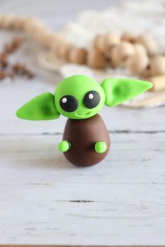 a small green toy sitting on top of a white wooden table next to some beads