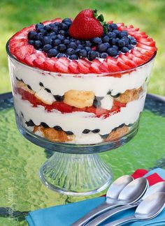 a cake with strawberries and blueberries in it on a glass plate next to silverware