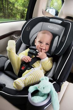 a baby sitting in a car seat holding a remote control and smiling at the camera