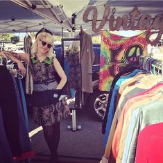 a woman standing in front of a tent with clothes hanging on the rack and other items behind her