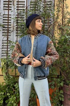 a woman standing in front of a bush with her hands on her hips wearing a denim jacket and plaid pants